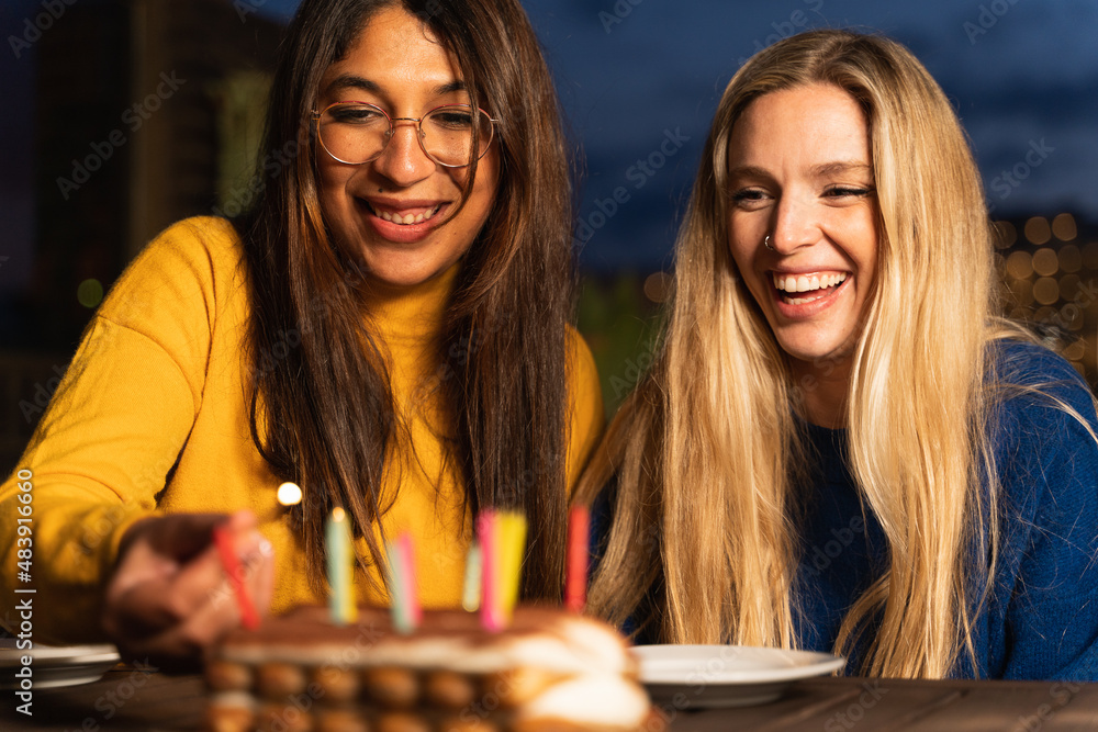 Fototapeta premium Cheerful women celebrating at home and lighting a birthday cake candles.