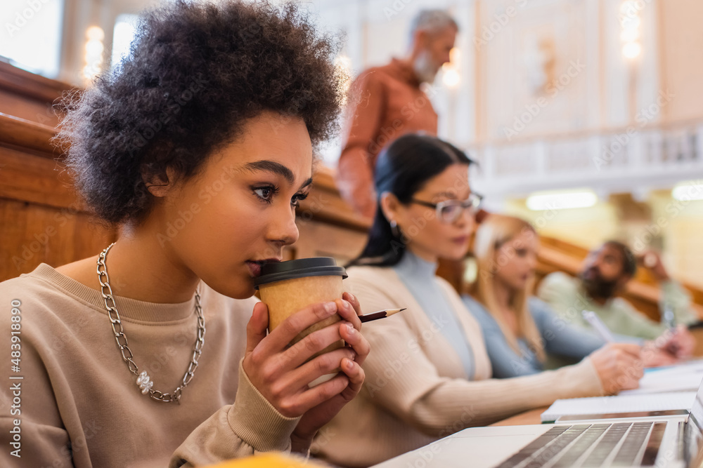 African american student holding coffee to go near laptop in university African american student holding coffee to go near laptop in university