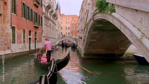 Gondola go down canal at day, Venice, Italy. Gondolier navigate boat. Tourists enjoy ride and take photos. Medieval buildings, channel waters 