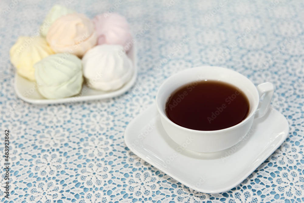 Traditional brewed tea in a cup and air marshmallows lie on table, a sweet dessert Traditional brewed tea in a cup and air marshmallows lie on table, a sweet dessert