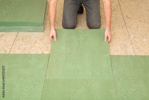 Man hands laying green natural wood fiber insulation board. Preparing surface from fibreboard underlay for laminate or parquet floor. Repair work of home. Renovation process. Closeup. Front view.