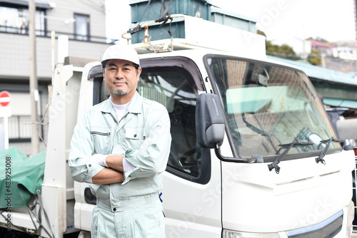 トラックの前で腕組みをする作業服を着たミドル男性