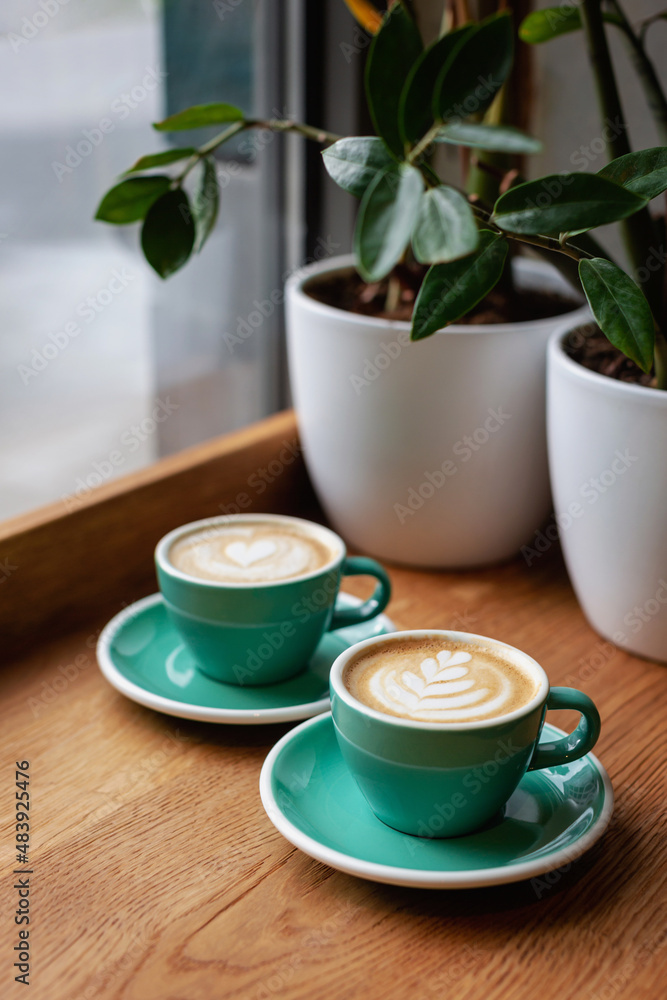 Two beautiful cups of cappuccino on the table. Decorated with perfect heart shape latte art. Coffee break, time in cafe, relax and enjoy the hot drink concept. Side view. Copy space for your text. Two beautiful cups of cappuccino on the table. Decorated with perfect heart shape latte art. Coffee break, time in cafe, relax and enjoy the hot drink concept. Side view. Copy space for your text.
