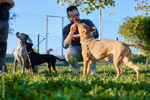 smiling young adult with sunglasses crouching down clicker training with his dog outdoors