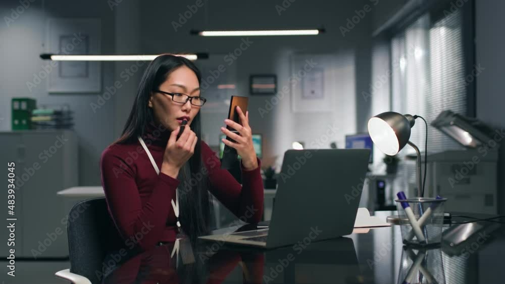 Businesswoman apply lipstick at desk in modern office Businesswoman apply lipstick at desk in modern office