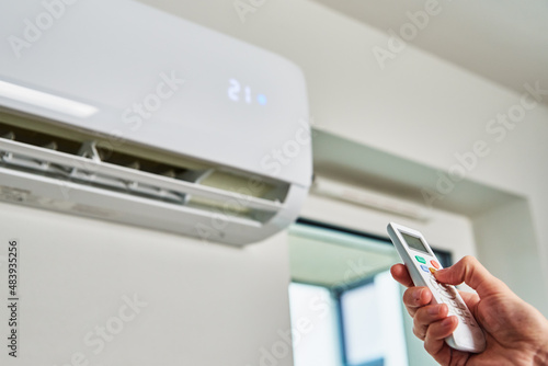 Hand adjusting temperature on air conditioner with remote control, Working air conditioner for comfort temperature in home at hot summer photo