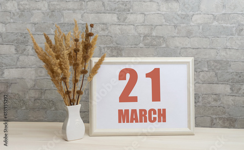 march 21. 21th day of month, calendar date.  White vase with ikebana and photo frame with numbers on desktop, opposite brick wall. Concept of day of year, time planner, spring month photo