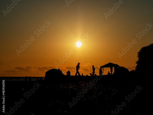 Silhouettes of people on the sea beach under the setting sun. Beach vacation at sunset