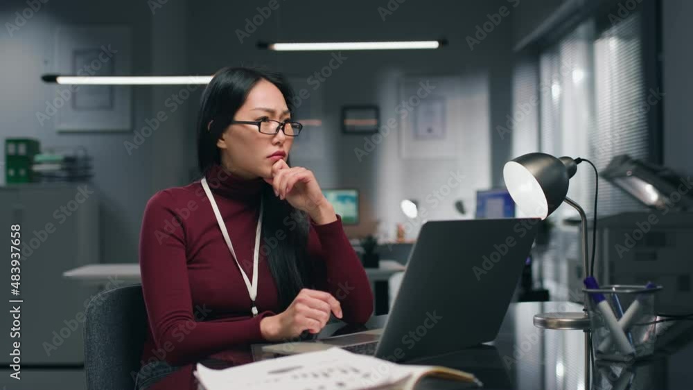 Tired pensive asian businesswoman sitting at desk and thinking in modern office Tired pensive asian businesswoman sitting at desk and thinking in modern office