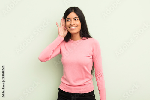 hispanic pretty woman smiling, looking curiously to the side, trying to listen to gossip or overhearing a secret photo