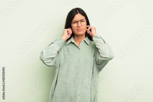 hispanic pretty woman looking angry, stressed and annoyed, covering both ears to a deafening noise, sound or loud music photo