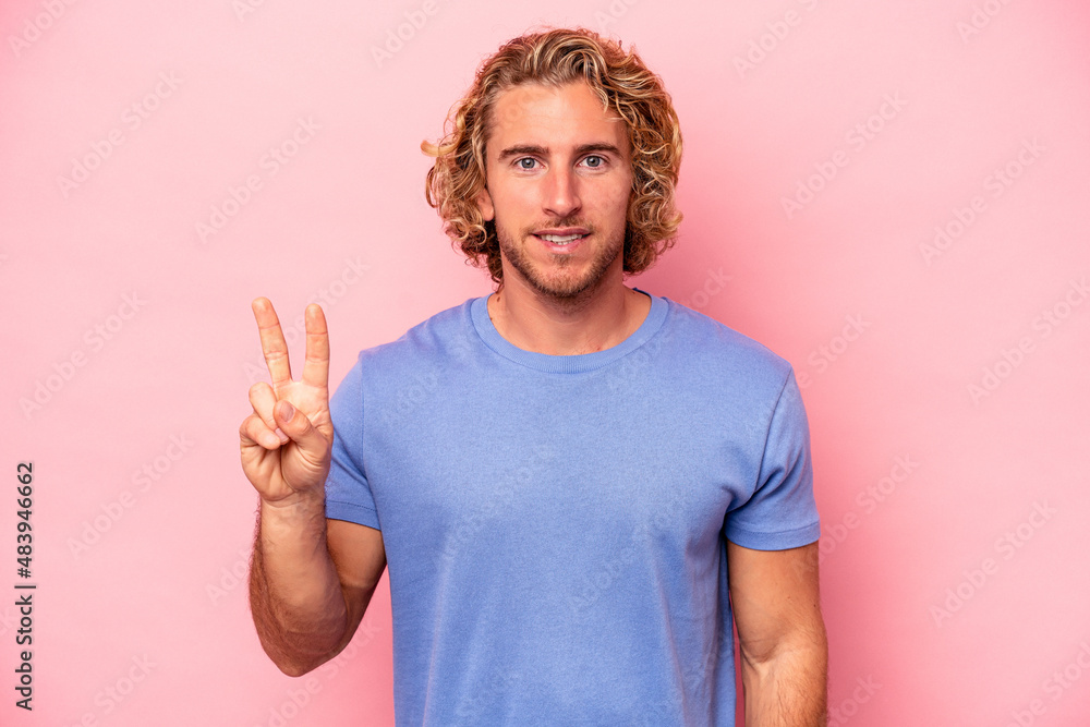 Young caucasian man isolated on pink background showing victory sign and smiling broadly. Young caucasian man isolated on pink background showing victory sign and smiling broadly.