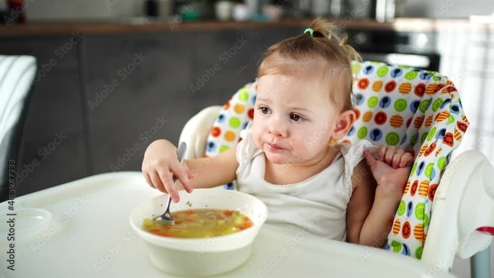 Cute baby girl toddler sitting in the high chair and eating her lunch soup at home kitchen. Cute baby girl toddler sitting in the high chair and eating her lunch soup at home kitchen.