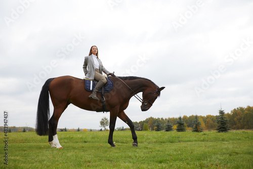 Beautiful young woman riding a horse on the field. Sideways to the camera. Freedom, joy, movement