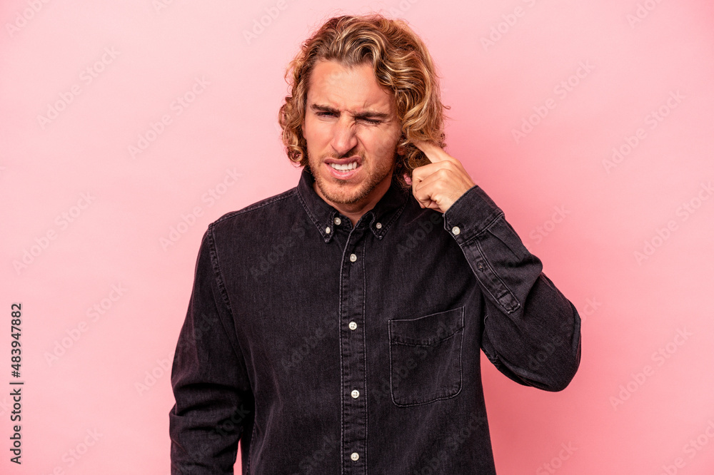 Young caucasian man isolated on pink background covering ears with fingers, stressed and desperate by a loudly ambient. Young caucasian man isolated on pink background covering ears with fingers, stressed and desperate by a loudly ambient.