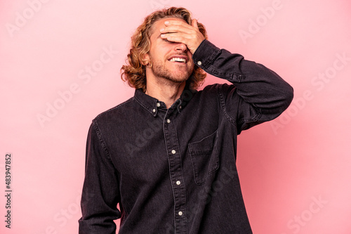 Young caucasian man isolated on pink background covers eyes with hands, smiles broadly waiting for a surprise. © Asier