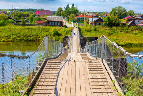 old picturesque wooden suspension bridge over the Tura river in the town of Verkhoturye on a summer sunny day photo