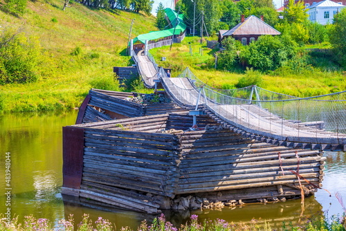 old picturesque wooden suspension bridge over the Tura river in the town of Verkhoturye on a summer sunny day photo