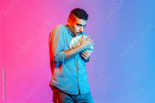 Fototapeta Man in shirt embracing dollar banknotes looking at camera with greedy expression, afraid to lose money, obsessed with finances