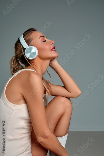 Banner of young happy girl in white swimsuit listening to music in white chair, wearing wireless headhones, isolated on gray background with copy space in studio photo