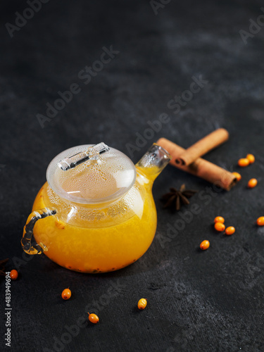 A teapot of sea buckthorn tea on a black table. Hot seasonal warming vitamin tea for colds