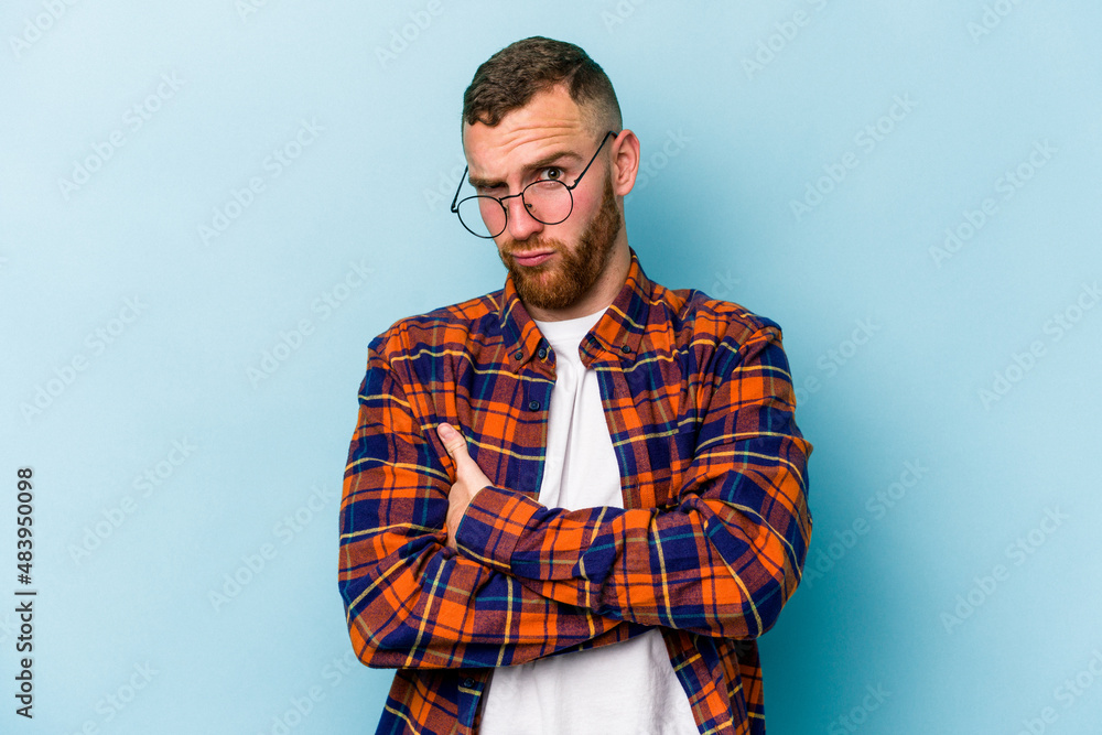 Fototapeta premium Young caucasian man isolated on blue background frowning face in displeasure, keeps arms folded.