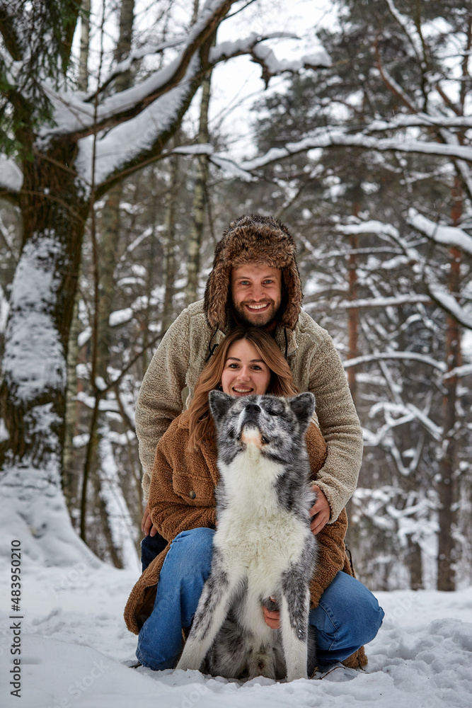 Young couple smiling and having fun in winter park with their husky dog Young couple smiling and having fun in winter park with their husky dog