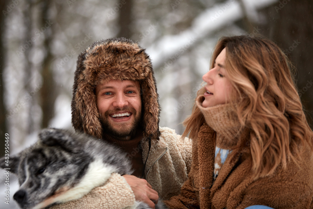 Young couple smiling and having fun in winter park with their husky dog Young couple smiling and having fun in winter park with their husky dog