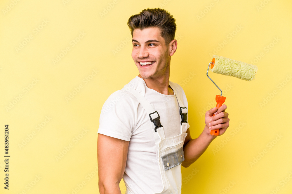 Young painter man isolated on yellow background looks aside smiling, cheerful and pleasant. Young painter man isolated on yellow background looks aside smiling, cheerful and pleasant.