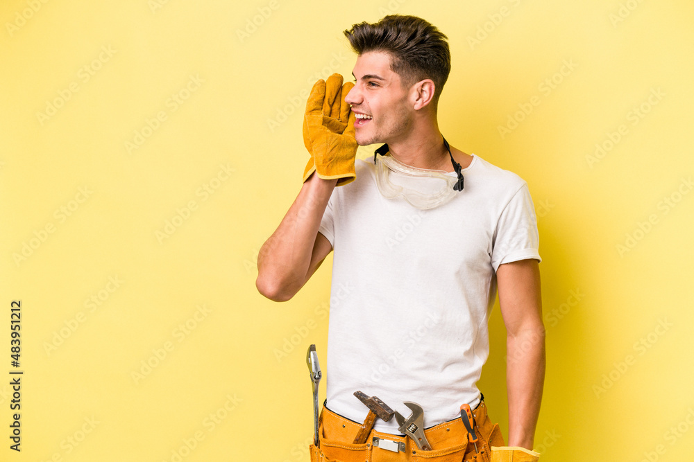 Young electrician caucasian man isolated on yellow background is saying a secret hot braking news and looking aside - obrazy, fototapety, plakaty 