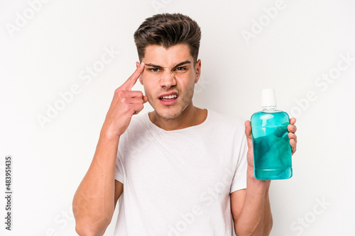 Young caucasian man holding mouthwash isolated on white background showing a disappointment gesture with forefinger.