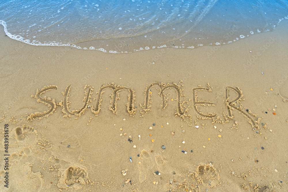 Fototapeta premium The word summer is written on the yellow sand of the beach. Blue wave and surf. Resort and vacation. Summer on the seaside. Relaxation rest concept.