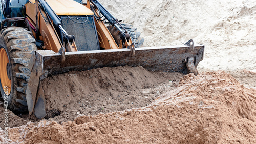 The excavator backfills the pit with the front bucket. Moves soil around the construction site. Close-up. Heavy construction equipment.