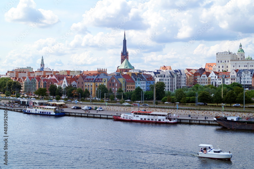 Panorama of the historical part of the city of Szczecin, the Odra River, on the pier of which there are ferries, ships, boats. Above the city a magnificent sunny sky with soft lush clouds