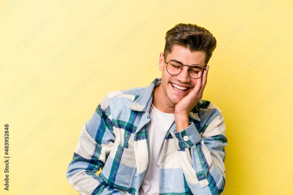Fototapeta premium Young caucasian man isolated on yellow background laughs happily and has fun keeping hands on stomach.