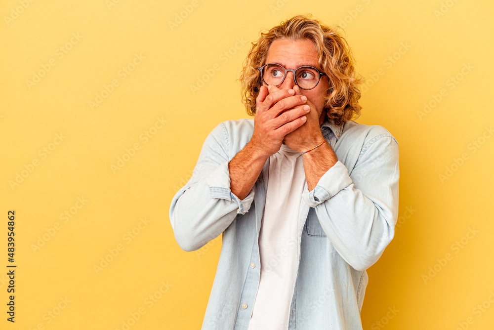 Young caucasian man isolated on yellow background thoughtful looking to a copy space covering mouth with hand. Young caucasian man isolated on yellow background thoughtful looking to a copy space covering mouth with hand.