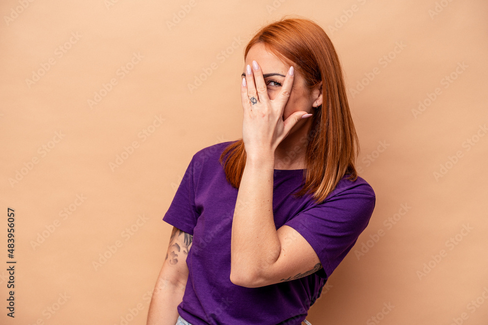 Young caucasian woman isolated on beige background blink at the camera through fingers, embarrassed covering face. Young caucasian woman isolated on beige background blink at the camera through fingers, embarrassed covering face.