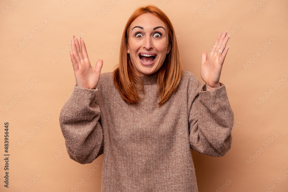 Young caucasian woman isolated on beige background receiving a pleasant surprise, excited and raising hands. Young caucasian woman isolated on beige background receiving a pleasant surprise, excited and raising hands.
