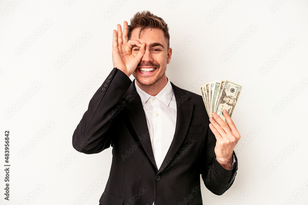 Young caucasian business man holding bank notes isolated on white background excited keeping ok gesture on eye. Young caucasian business man holding bank notes isolated on white background excited keeping ok gesture on eye.