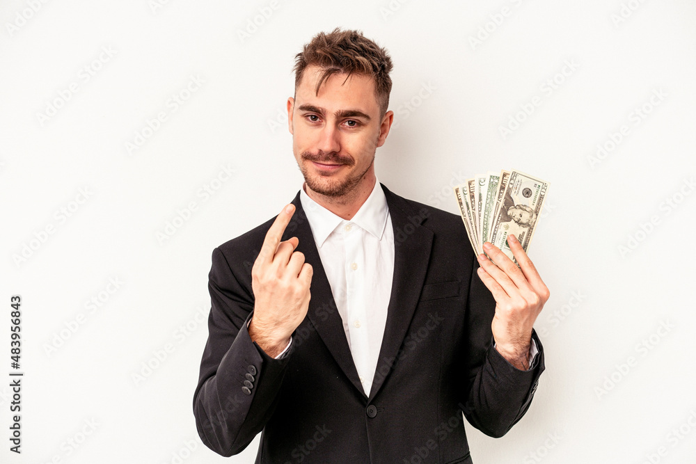 Young caucasian business man holding bank notes isolated on white background pointing with finger at you as if inviting come closer. Young caucasian business man holding bank notes isolated on white background pointing with finger at you as if inviting come closer.