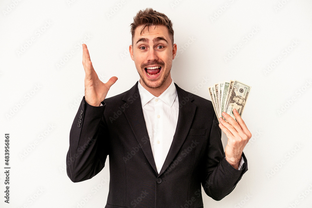 Young caucasian business man holding bank notes isolated on white background receiving a pleasant surprise, excited and raising hands. Young caucasian business man holding bank notes isolated on white background receiving a pleasant surprise, excited and raising hands.