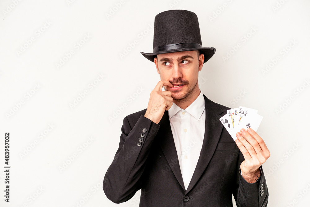 Young caucasian wizard man holding a magic cards isolated on white background relaxed thinking about something looking at a copy space. Young caucasian wizard man holding a magic cards isolated on white background relaxed thinking about something looking at a copy space.