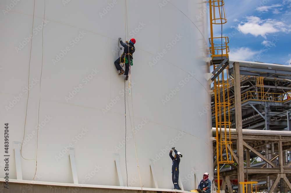 Male workers control rope down height tank rope access inspection of thickness shell plate tank.