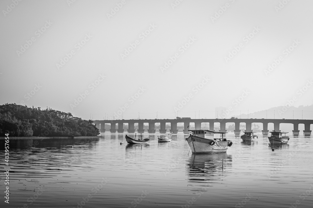 Barcos de pesca ancorados no mar e ao fundo uma ponte 