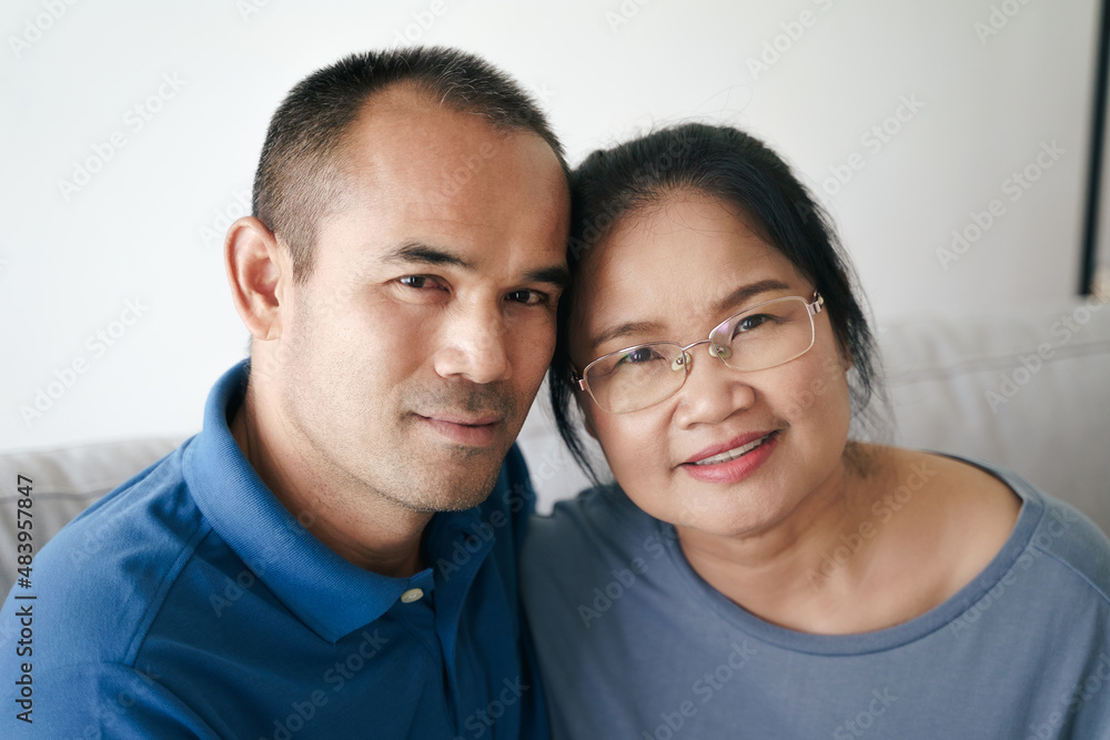Portrait of Asian mature couple sitting in the living room. wife and husband hugging, holding hand with happiness and cheerful. Love, safety, and insurance family concept. Portrait of Asian mature couple sitting in the living room. wife and husband hugging, holding hand with happiness and cheerful. Love, safety, and insurance family concept.