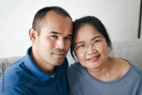 Portrait of Asian mature couple sitting in the living room. wife and husband hugging, holding hand with happiness and cheerful. Love, safety, and insurance family concept.