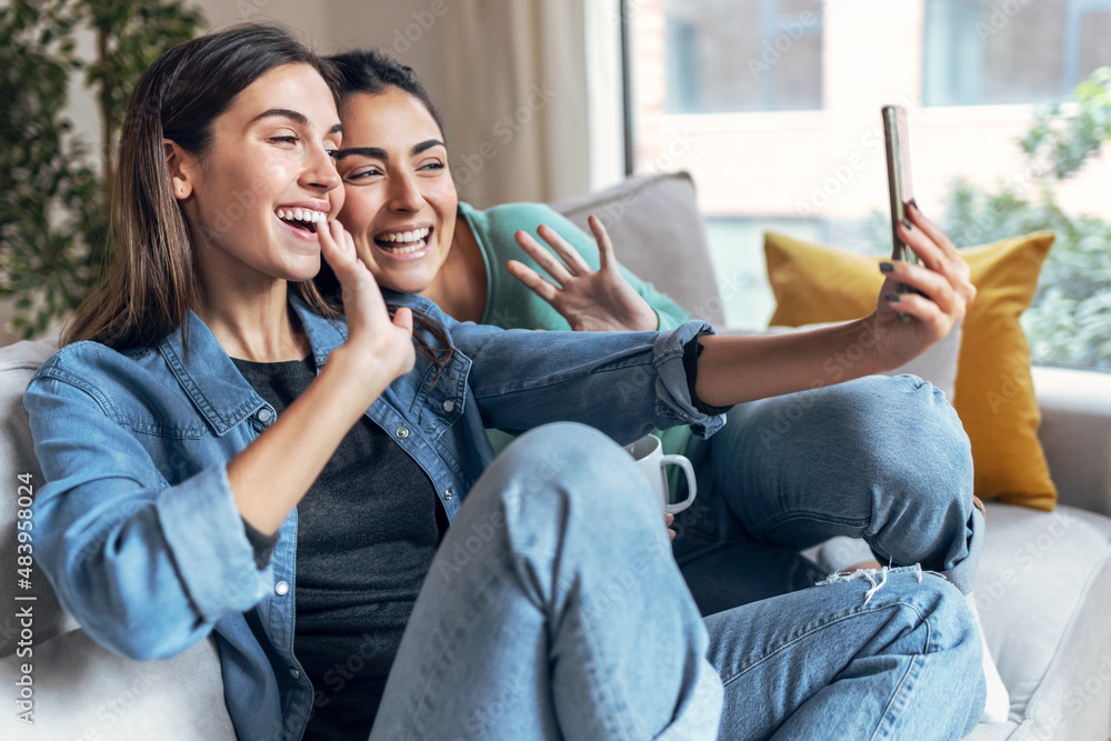 Two happy beautiful women doing a video call with laptop sitting on the ...