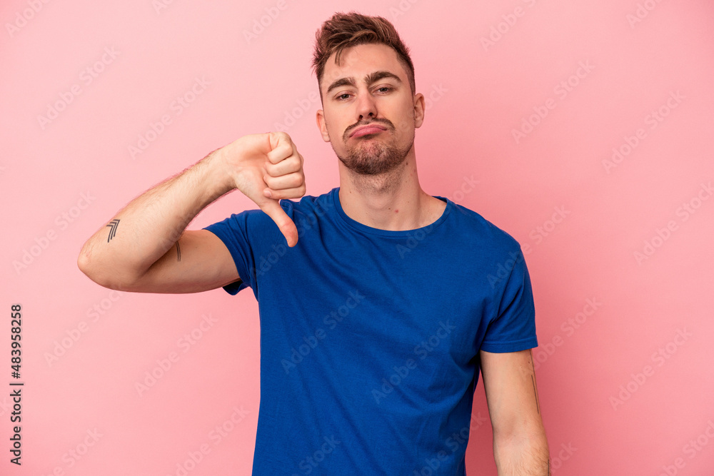 Young caucasian man isolated on pink background showing thumb down and expressing dislike. Young caucasian man isolated on pink background showing thumb down and expressing dislike.