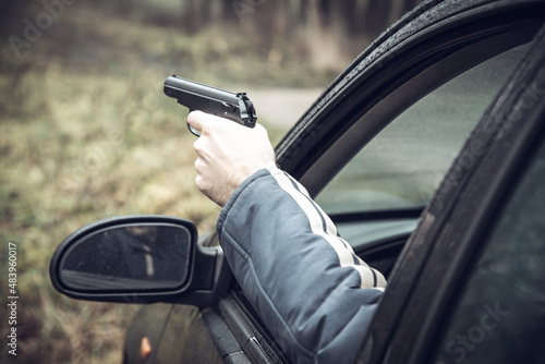 A man with a gun driving a car, a man's hand with a gun in his hand leaned out of the car window photo