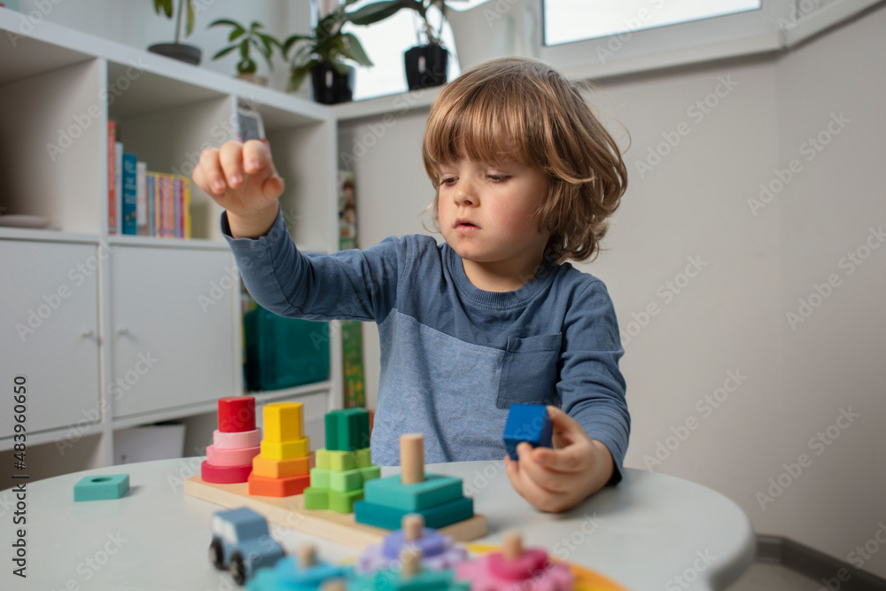 Beautiful toddler play with a wooden toys at home. Toddler play with a color educational toy and wooden car. Child play at the table in the baby room. Funny baby. Lifestyle.